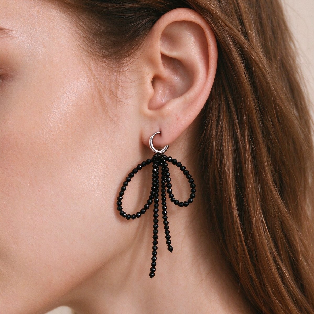 Model wearing 7.5cm black tourmaline bow drop earrings in autumn street style